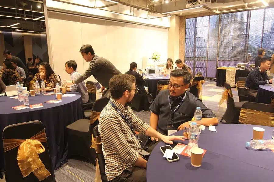 Attendees seated at round tables in a room with tall windows at a previous SCALECON