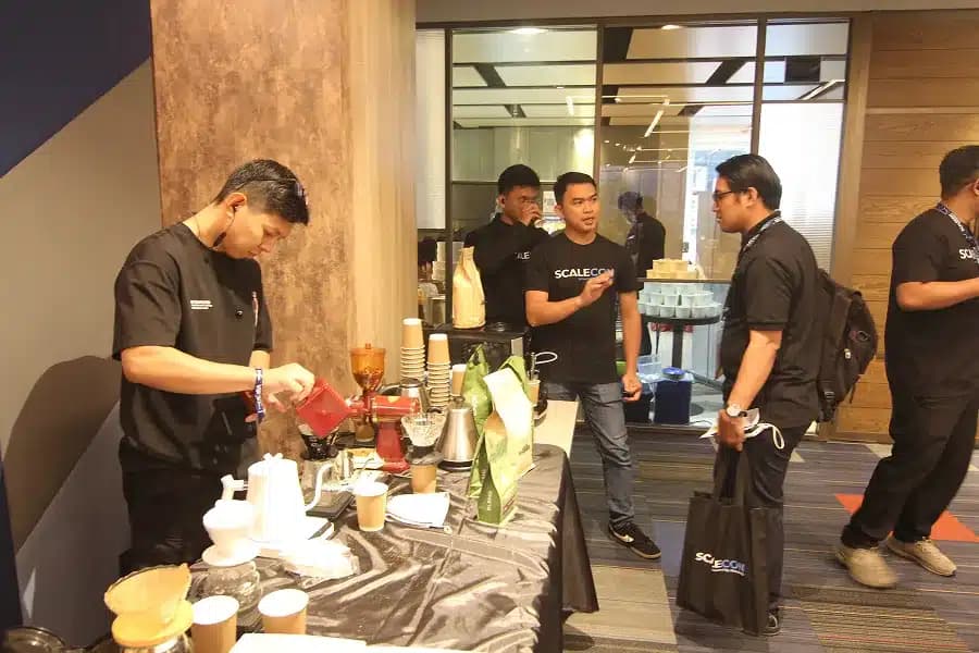 Staff preparing coffee while attendees pass the counter at a previous SCALECON